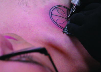 Trevor Yokochi sits as an artist carefully fills in the design on his tattoo.