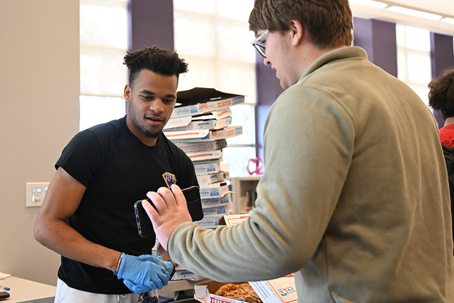 Senior Dontarious Johnson hands out pizza to junior Ethan Klausing at the CTE fair in the library. Photo credit: Shea Southern