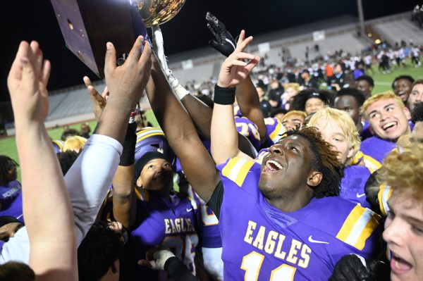 Junior defensive end Antrell Smith-Bowen holds up the 6A Bi-District Championship trophy as the rest of the team celebrates. The varsity football team defeated Haltom 35-7 marking their first back-to-back Bi-District Championship title since 1991. Round two will be against Coppell High School on Nov. 20. Talon photo by Ray Brosnahan